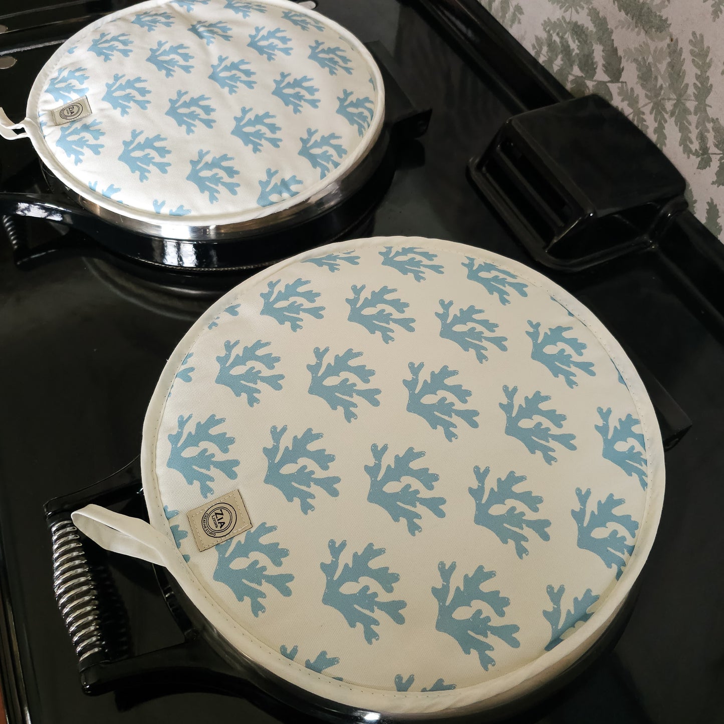 Blue seaweed print Aga and hob pair of covers by ZIA LIVING, featuring a white coral motif on a deep‑blue cotton base, shown on a glossy black stove with metal handles.