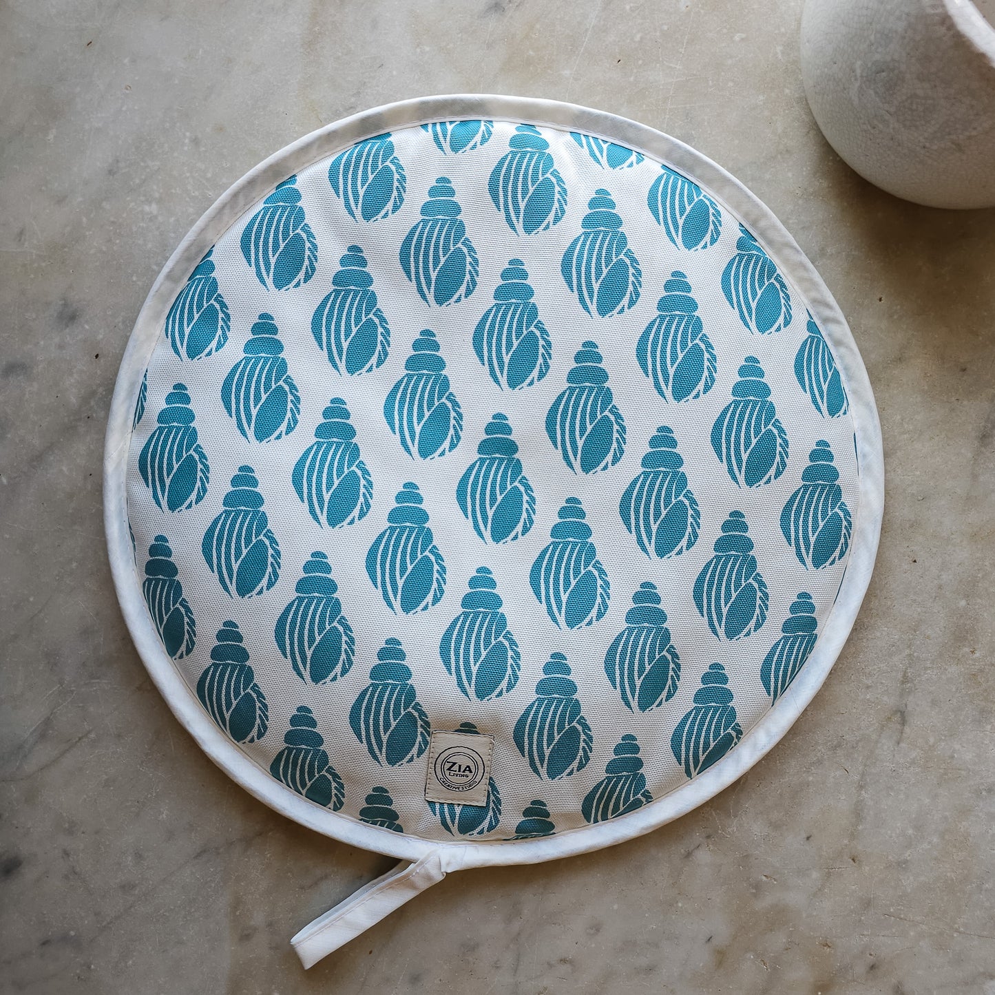 Sea Blue Shell round Aga and hob cover by ZIA LIVING, featuring a blue shell lino‑print pattern on cotton with fabric ties, shown on marble worktop