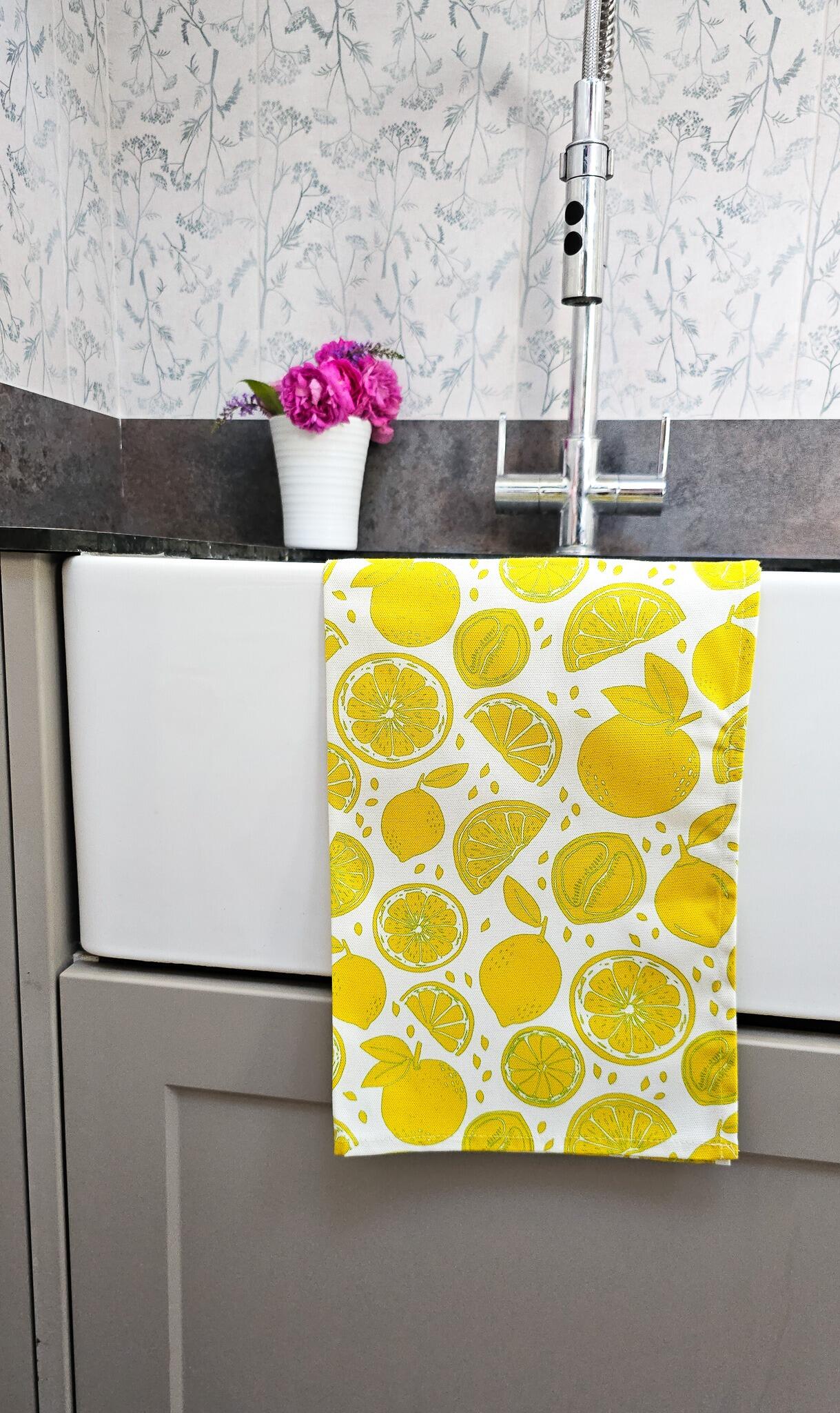 Lemon patterned tea towel folded over a sink in a kitchen with vase of pink flowers— ZIA LIVING