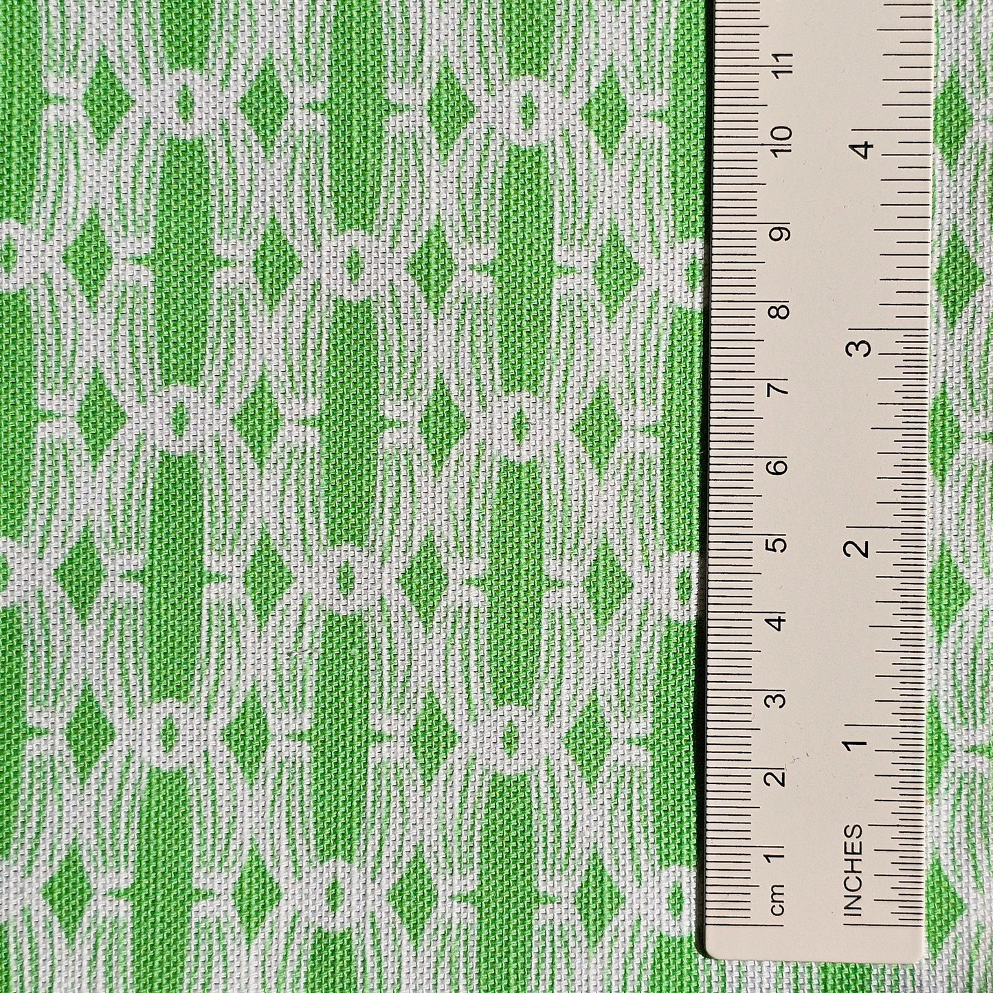 Close‑up of ZIA LIVING’s Anello cotton‑linen fabric in apple green and white, showing its interlocking oval and diamond geometric weave pattern and textured artisan finish. With ruler showing scale of pattern repeat.