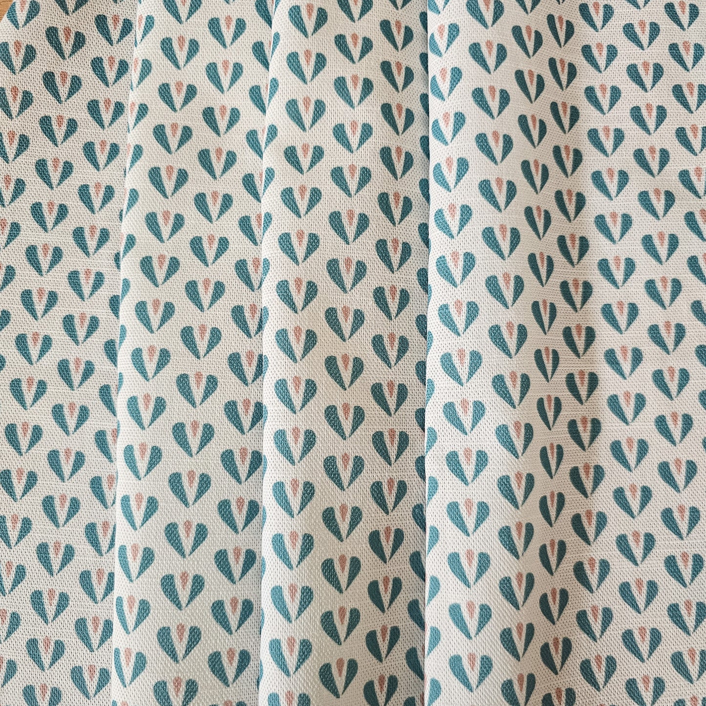 Carina, heart shaped motif in duck egg and pink colours on neutral fabric, shown as drapes, by Zia Living