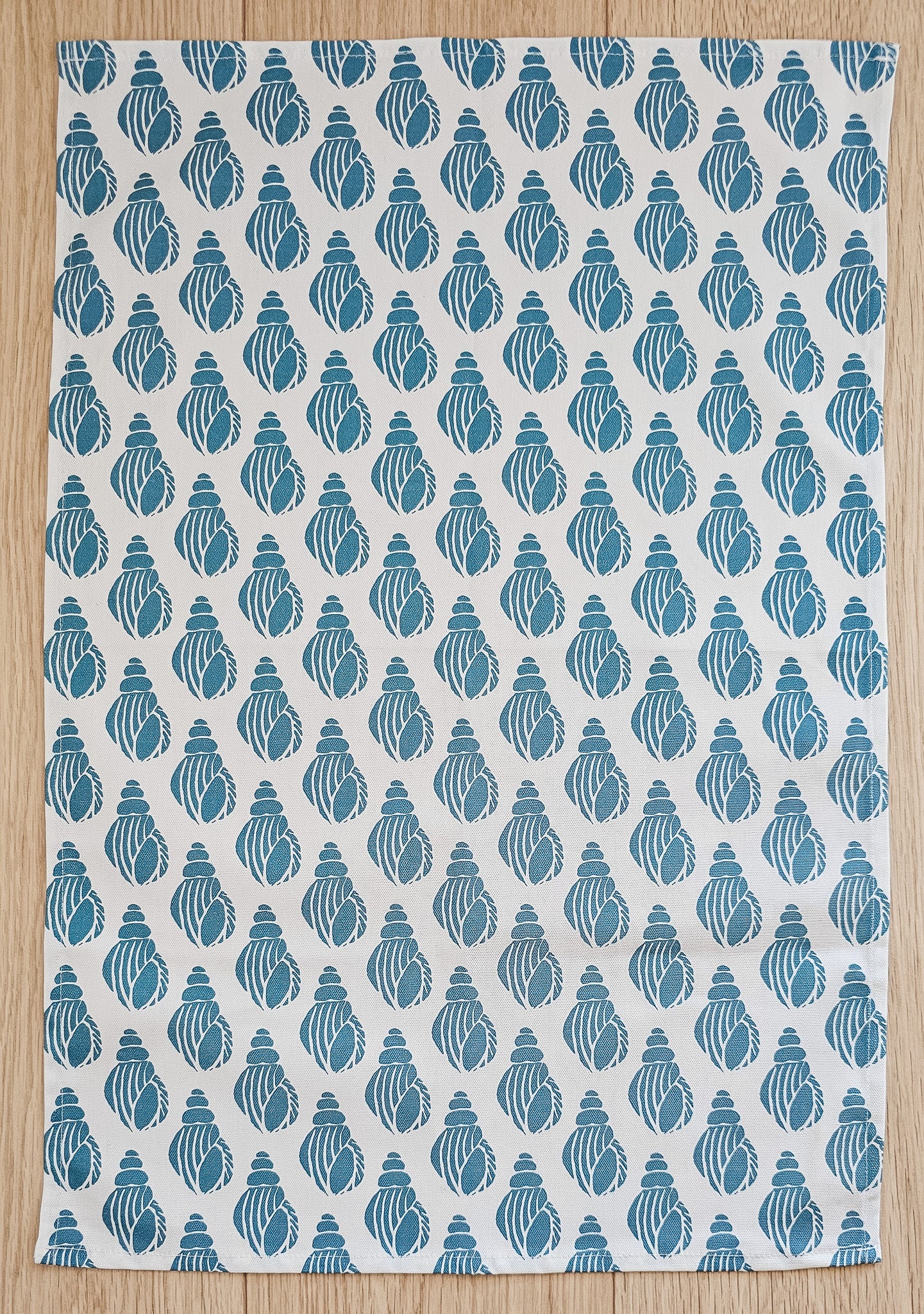 A Shell print tea towel from ZIA LIVING laid flat on wooden worktop showing full design