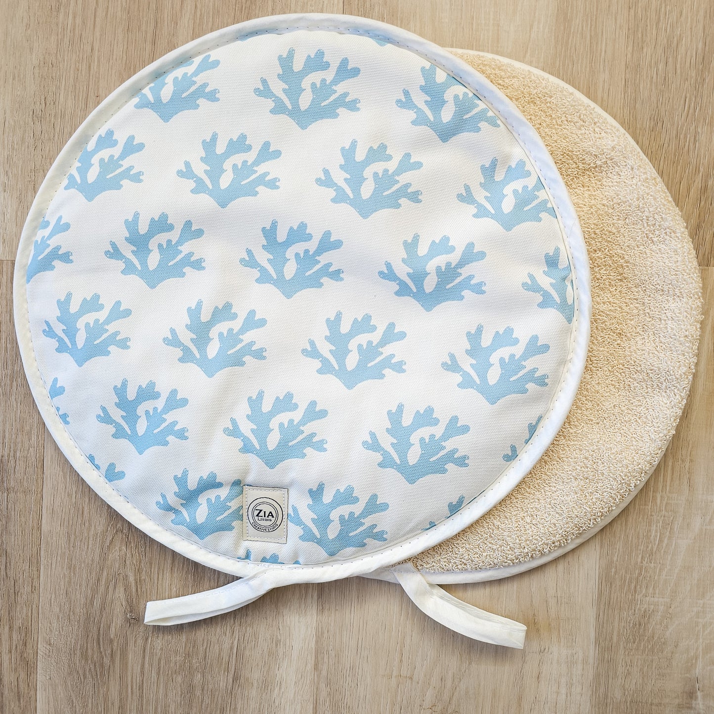 A Seaweed print in sky blue aga pad showing the patterned front and plain reverse laid on a wooden surface by Zia-Living