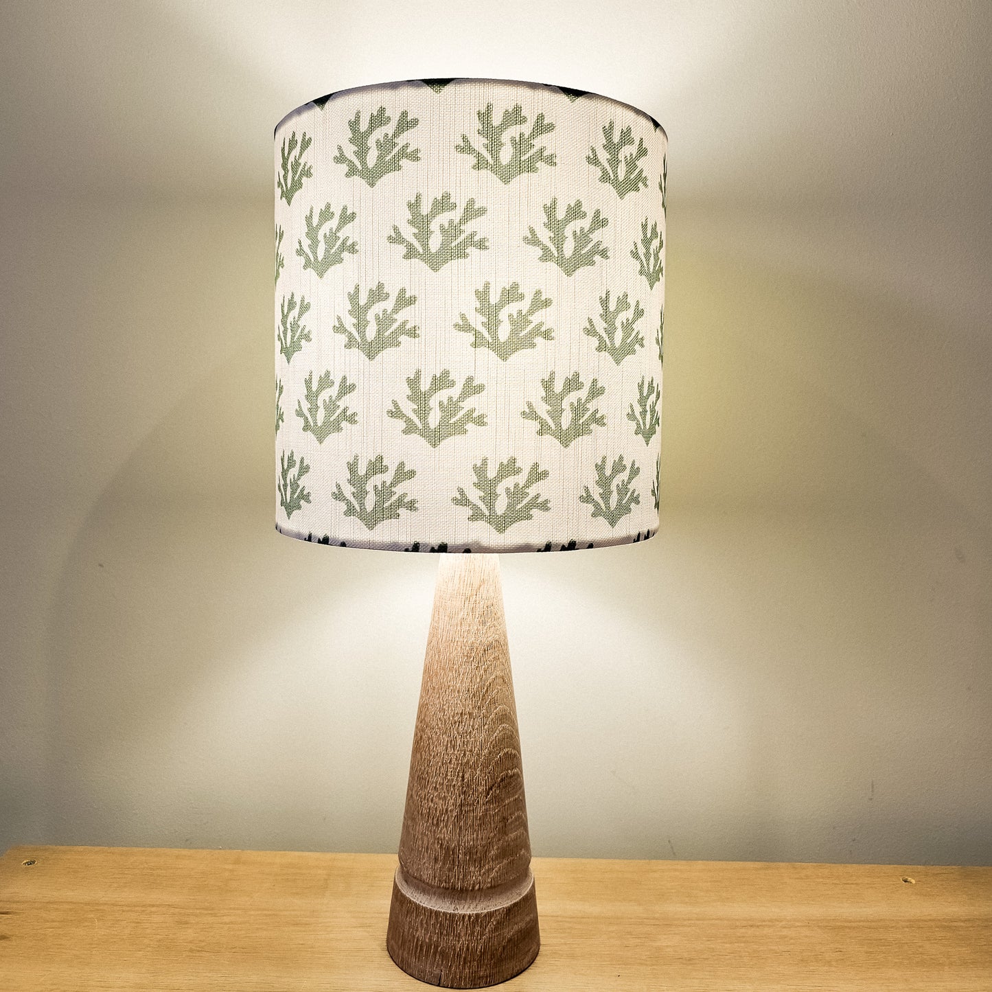 Handmade drum lampshade in green seaweed‑print fabric on a wooden lamp base, glowing softly against a neutral wall — artisan home décor by ZIA LIVING