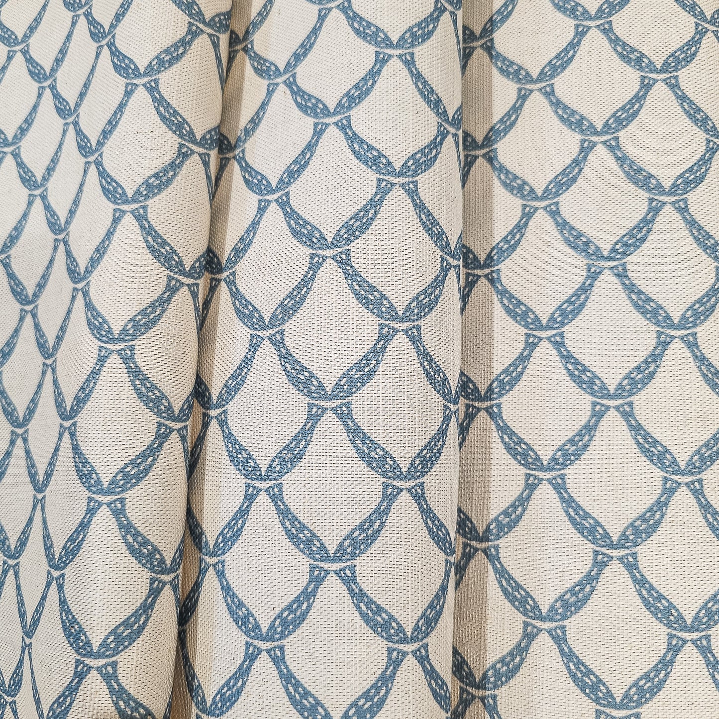Marina cotton linen fabric folds featuring an interlocking curved blue lattice pattern on an natural background. ZIA LIVING