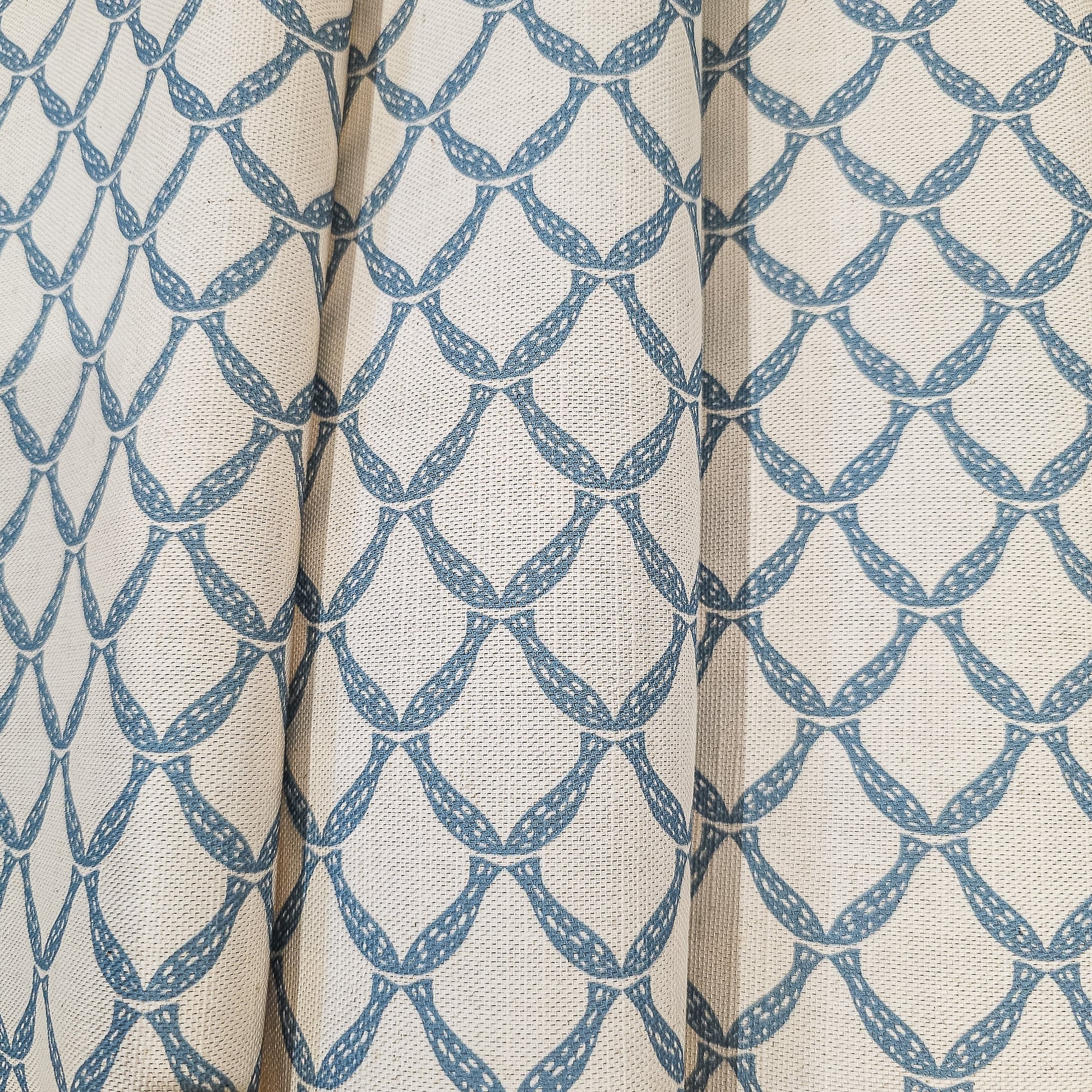 Marina cotton linen fabric folds featuring an interlocking curved blue lattice pattern on an natural background. ZIA LIVING
