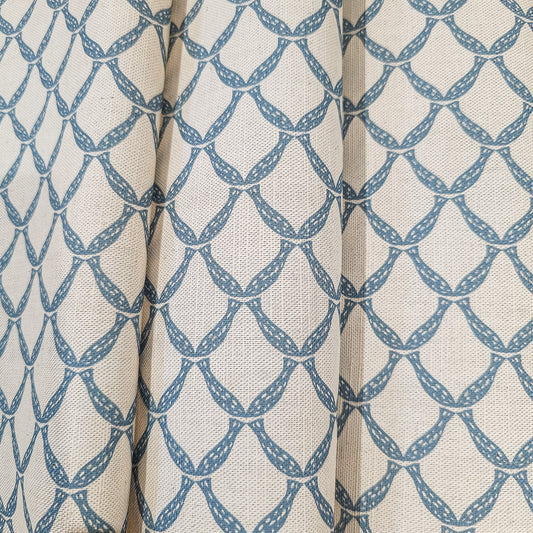 Marina cotton linen fabric folds featuring an interlocking curved blue lattice pattern on an natural background. ZIA LIVING