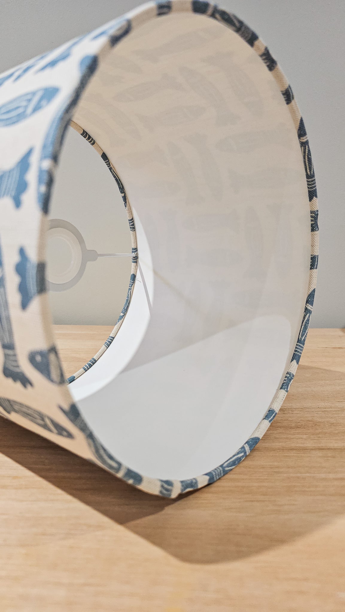 Blue Fishes drum lampshade featuring simple hand‑drawn fish motifs on a warm neutral background, lampshade shape, styled on a wooden surface — ZIA LIVING.
