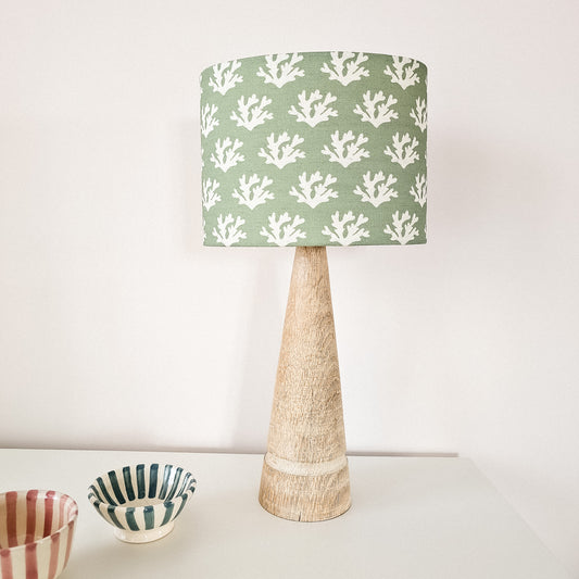 Green Seaweed drum lampshade with white coral‑inspired motifs on a textured lamp base, styled beside a small striped