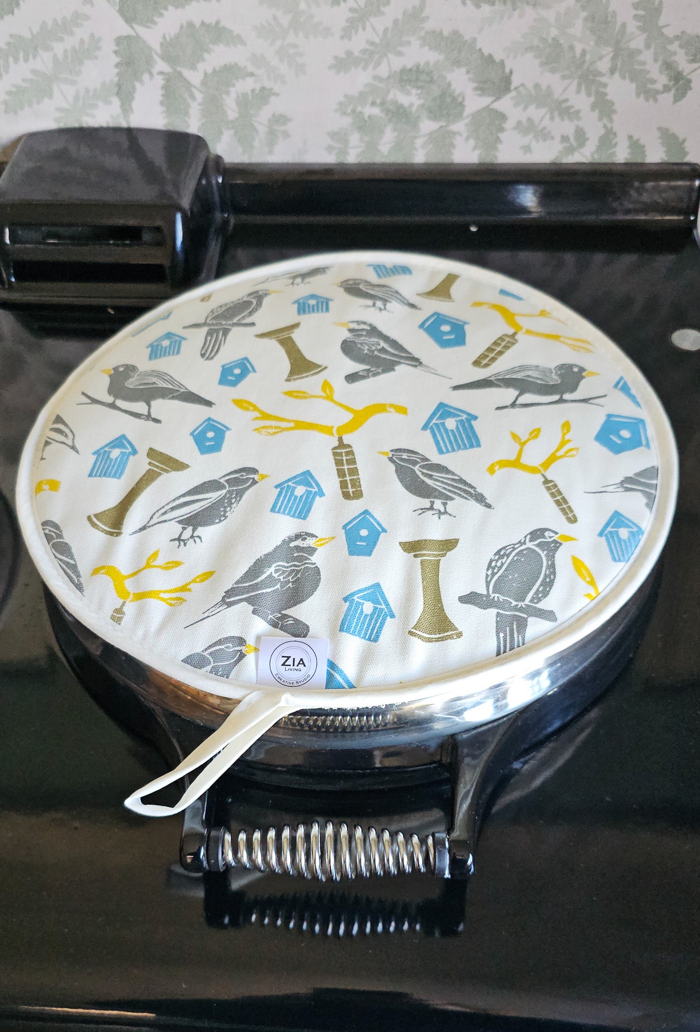 Bird House print round aga hob cover by ZIA LIVING, featuring illustrated birds, birdhouses and branches in soft grey, blue and yellow tones, shown on a aga back hob