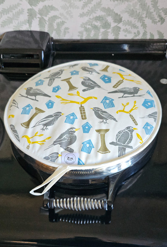 Bird House print round aga hob cover by ZIA LIVING, featuring illustrated birds, birdhouses and branches in soft grey, blue and yellow tones, shown on a aga back hob