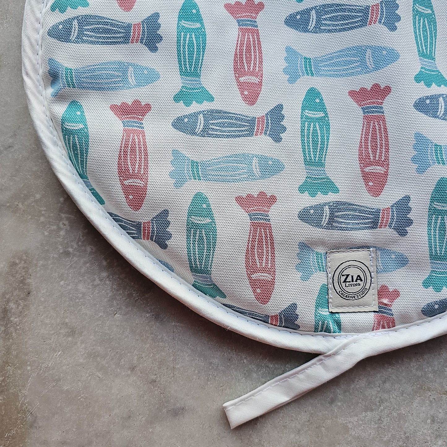 Fish print round kitchen cover by ZIA LIVING, featuring a repeating red, teal and light‑blue fish motif close up on marble worktop