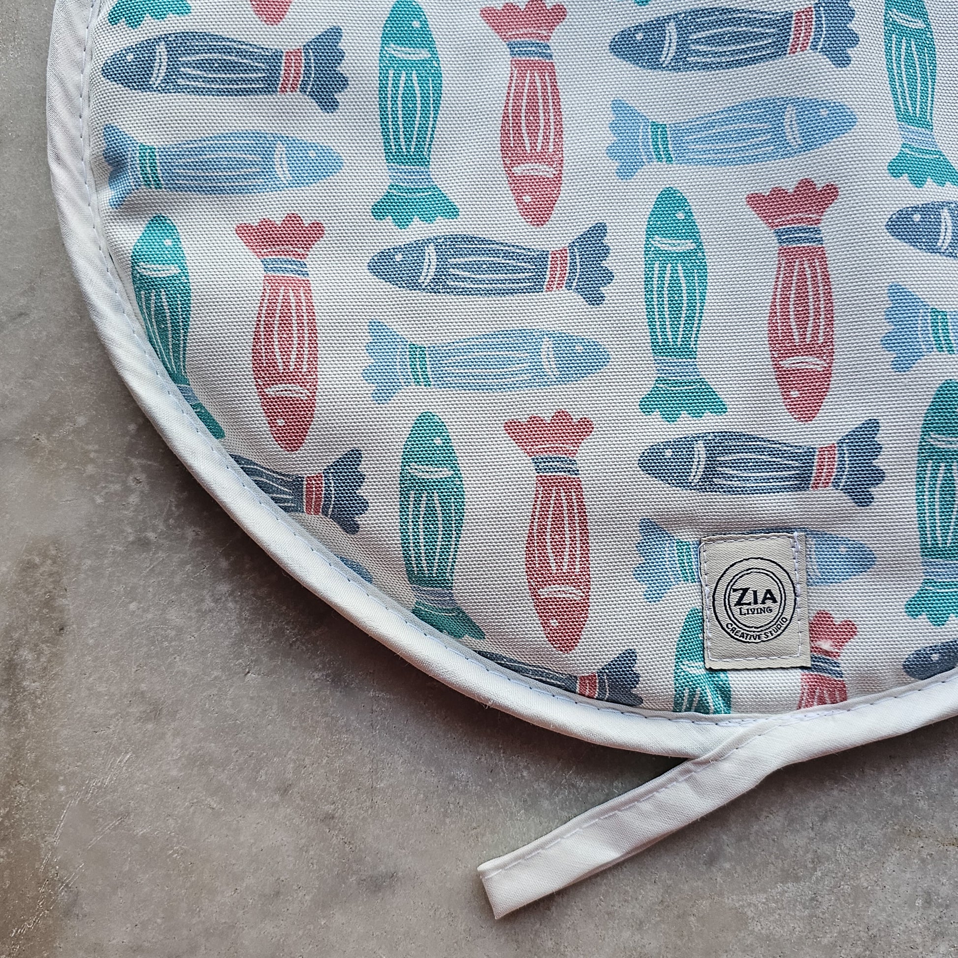 Fish print round kitchen cover by ZIA LIVING, featuring a repeating red, teal and light‑blue fish motif close up on marble worktop