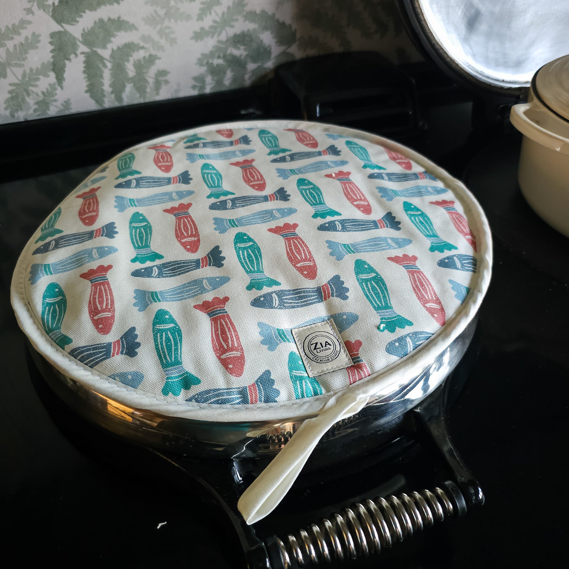 Fish print round kitchen cover by ZIA LIVING, featuring a repeating red, teal and light‑blue fish motif on cotton‑linen, shown on aga hob