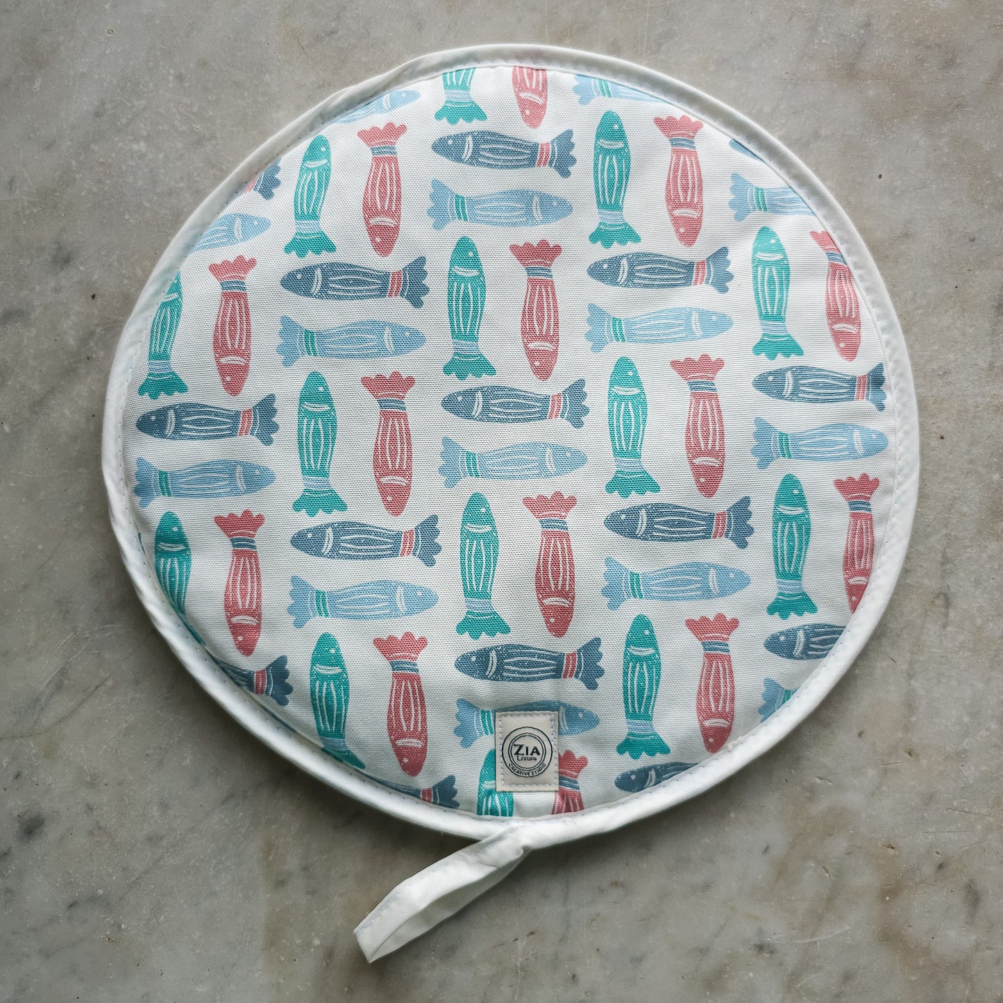 Fish print round kitchen cover by ZIA LIVING, featuring a repeating red, teal and light‑blue fish motif on cotton‑linen, shown on marble top
