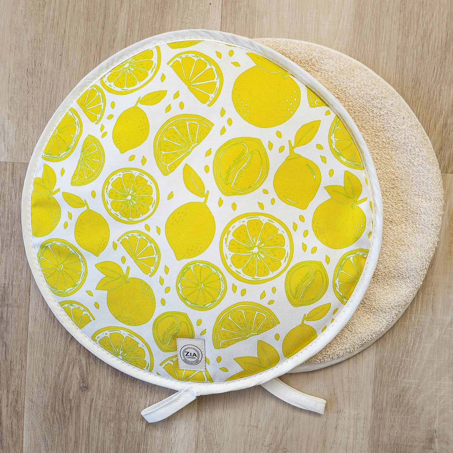 Lemon print round aga hob cover by ZIA LIVING, featuring bright yellow citrus fruit motifs on cotton, with ties and towelling reverse on wooden worktop