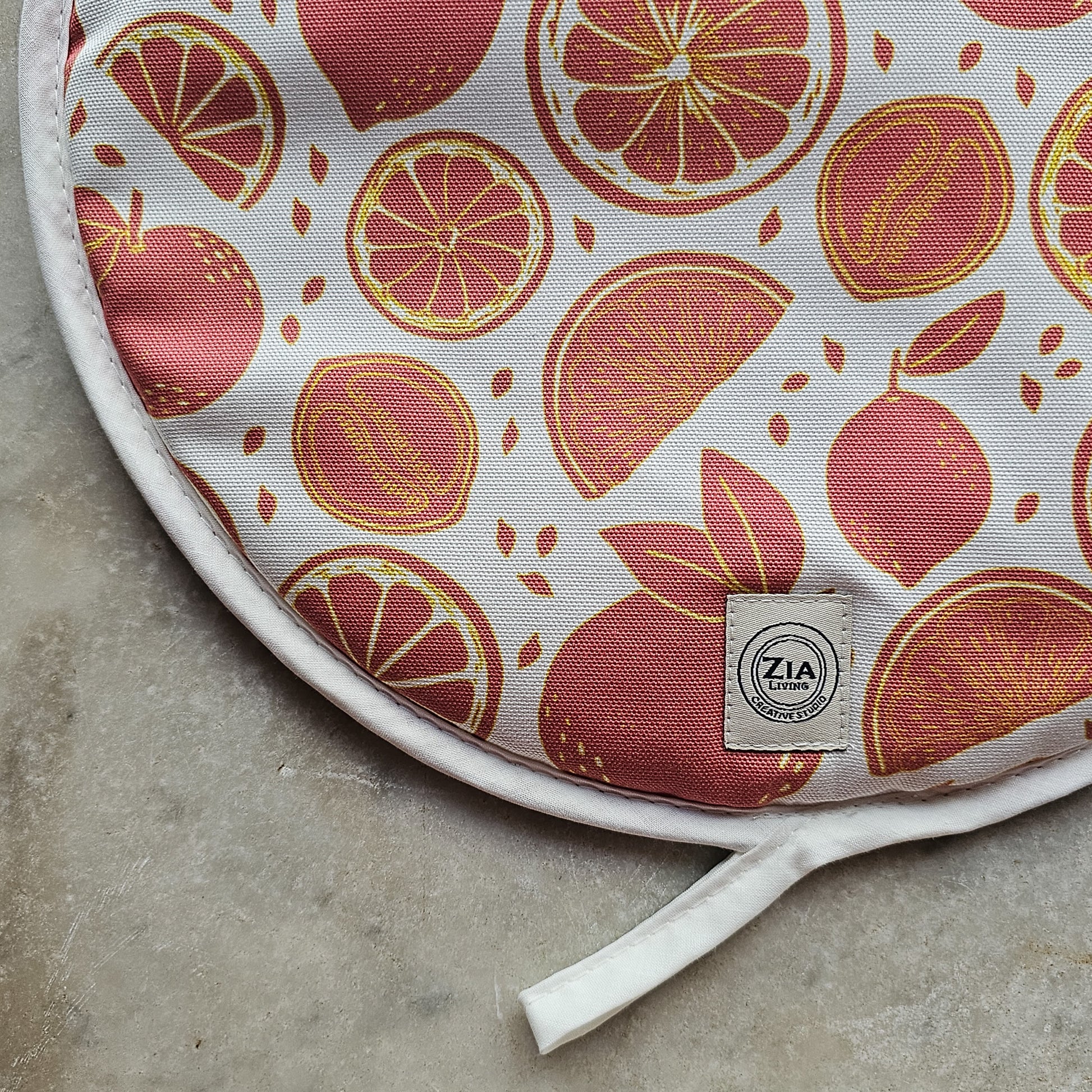 Close up of orange Citrus print round hob cover by ZIA LIVING, featuring orange and grapefruit motifs on a white cotton base, shown on white marble worktop
