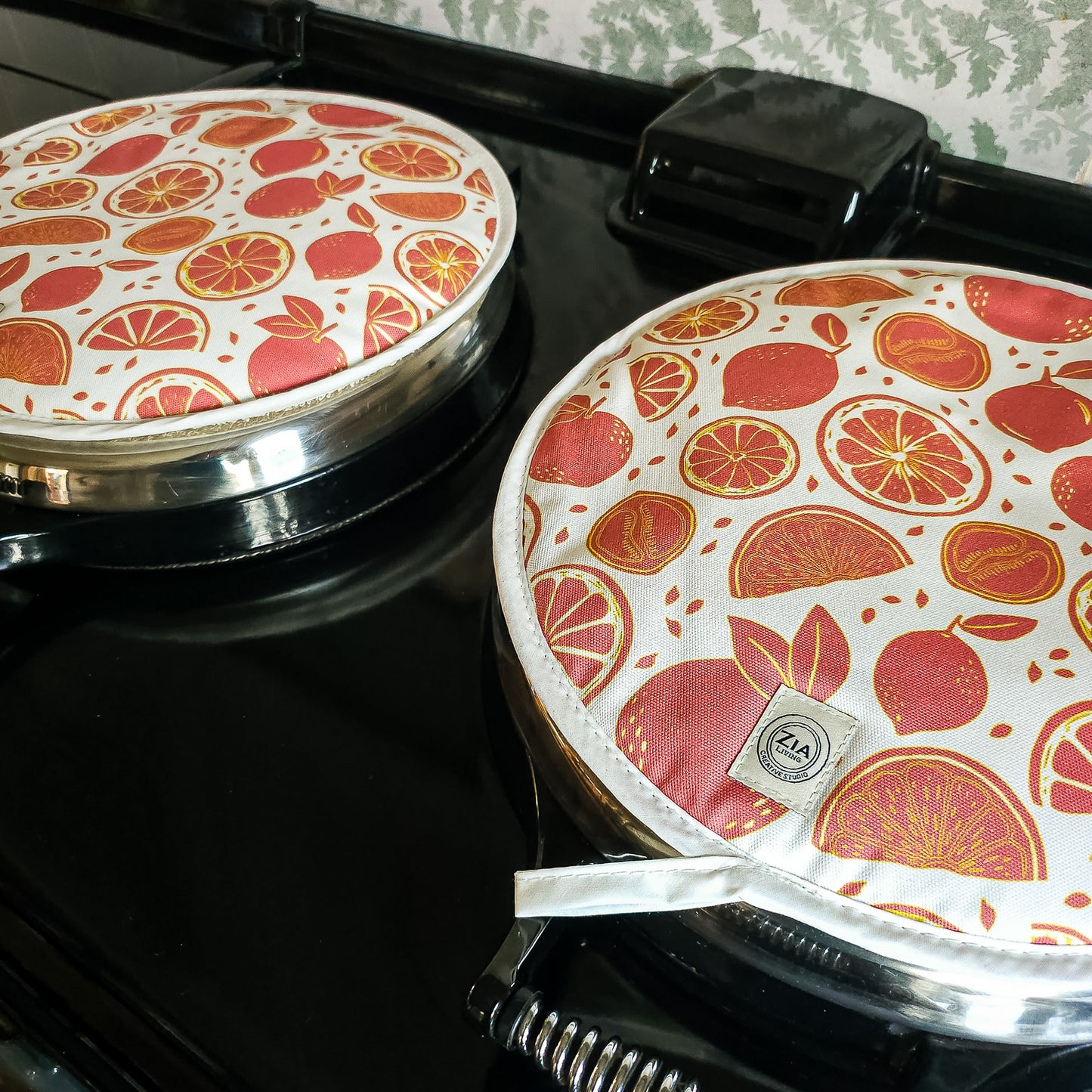 pair of orange Citrus print round hob cover by ZIA LIVING, featuring orange and grapefruit motifs on a white cotton base, shown on aga hob.