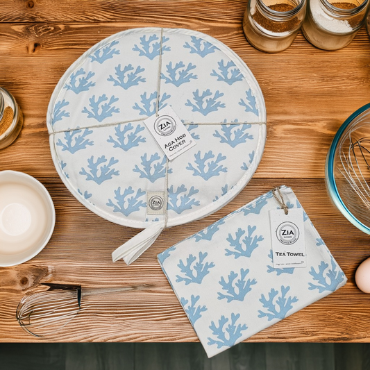 A round Seaweed print aga hob cover and matching tea towel from ZIA LIVING arranged on a wooden countertop alongside bowls, jars, and baking utensils.