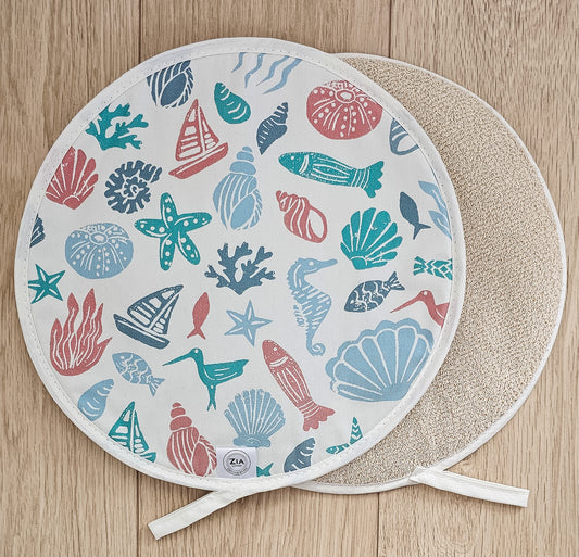 Under the Sea round Aga and hob cover by ZIA LIVING, featuring a colourful coastal lino‑print pattern with sea creatures, shells and boats on cotton, shown with a natural textured underside on a wooden surface.