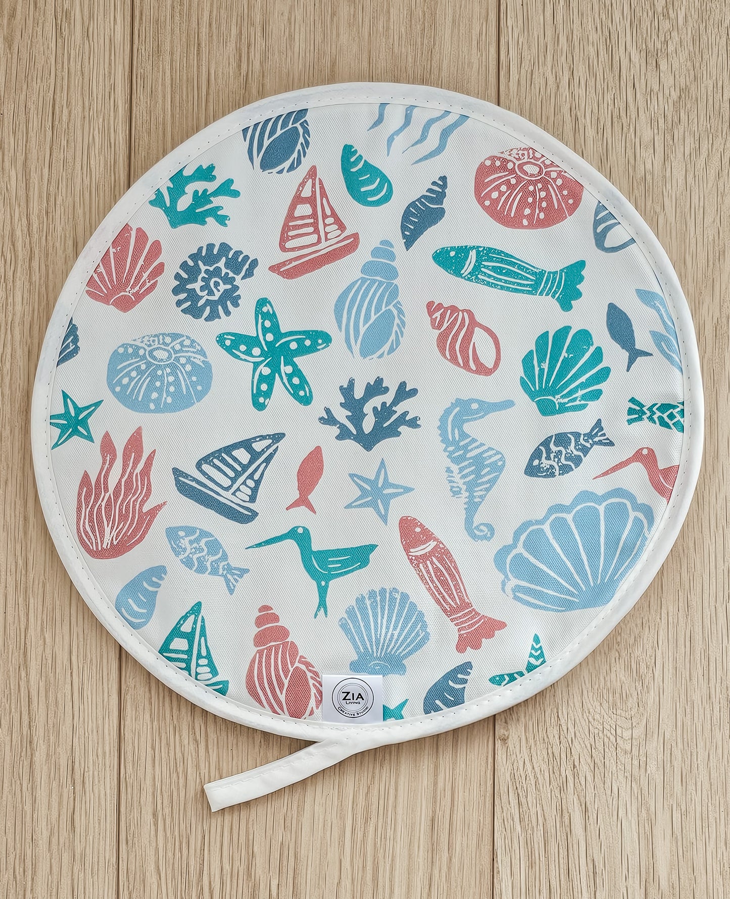 Under the Sea round Aga and hob cover by ZIA LIVING, featuring a colourful coastal lino‑print pattern with sea creatures, shells and boats on cotton, shown on a wooden surface.
