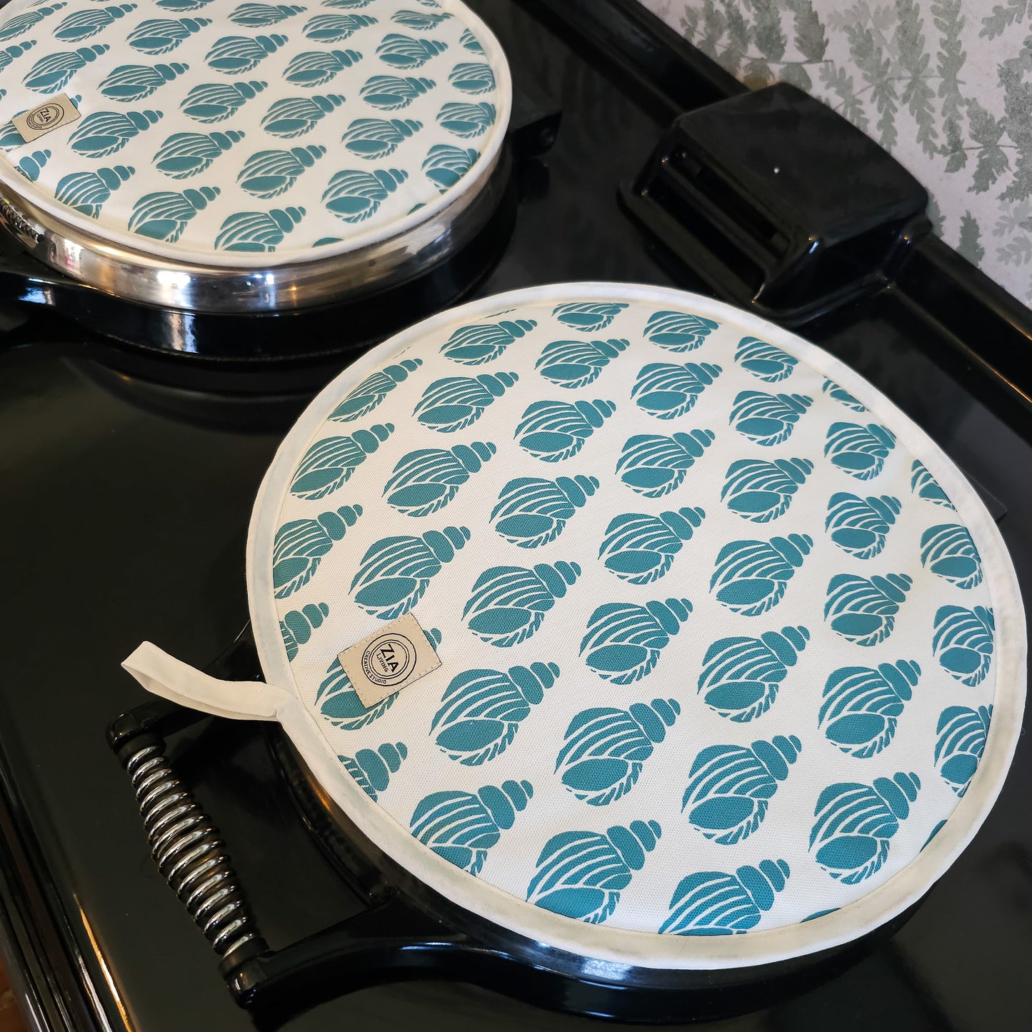 Sea Blue Shell round Aga and hob cover by ZIA LIVING, featuring a blue shell lino‑print pattern on cotton with fabric loop, pair of covers shown on aga.