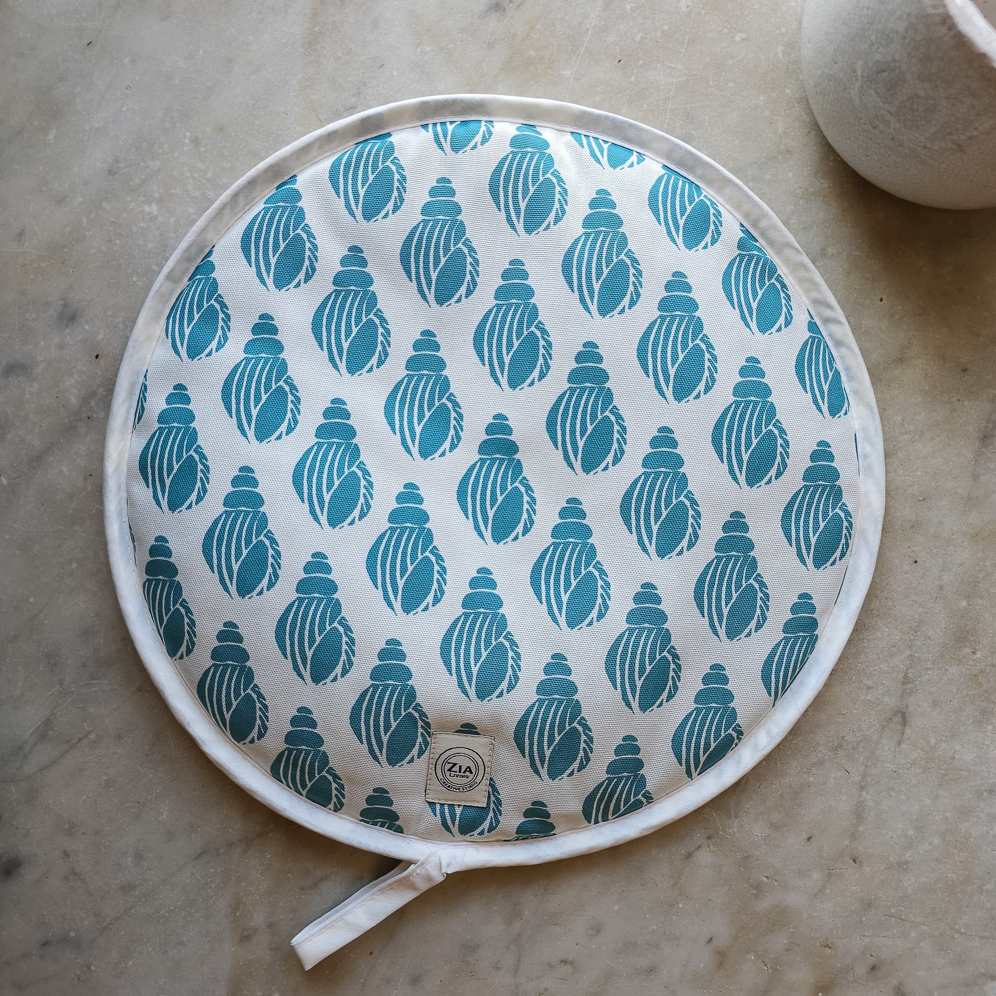 Sea Blue Shell round Aga and hob cover by ZIA LIVING, featuring a blue shell lino‑print pattern on cotton with fabric ties, shown on marble worktop