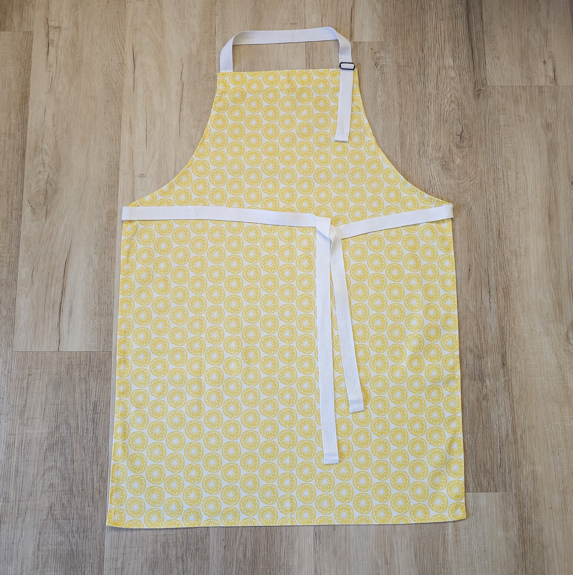 Yellow Seedhead apron featuring a yellow circular botanical motif, laid flat with white ties on wooden background— ZIA LIVING.