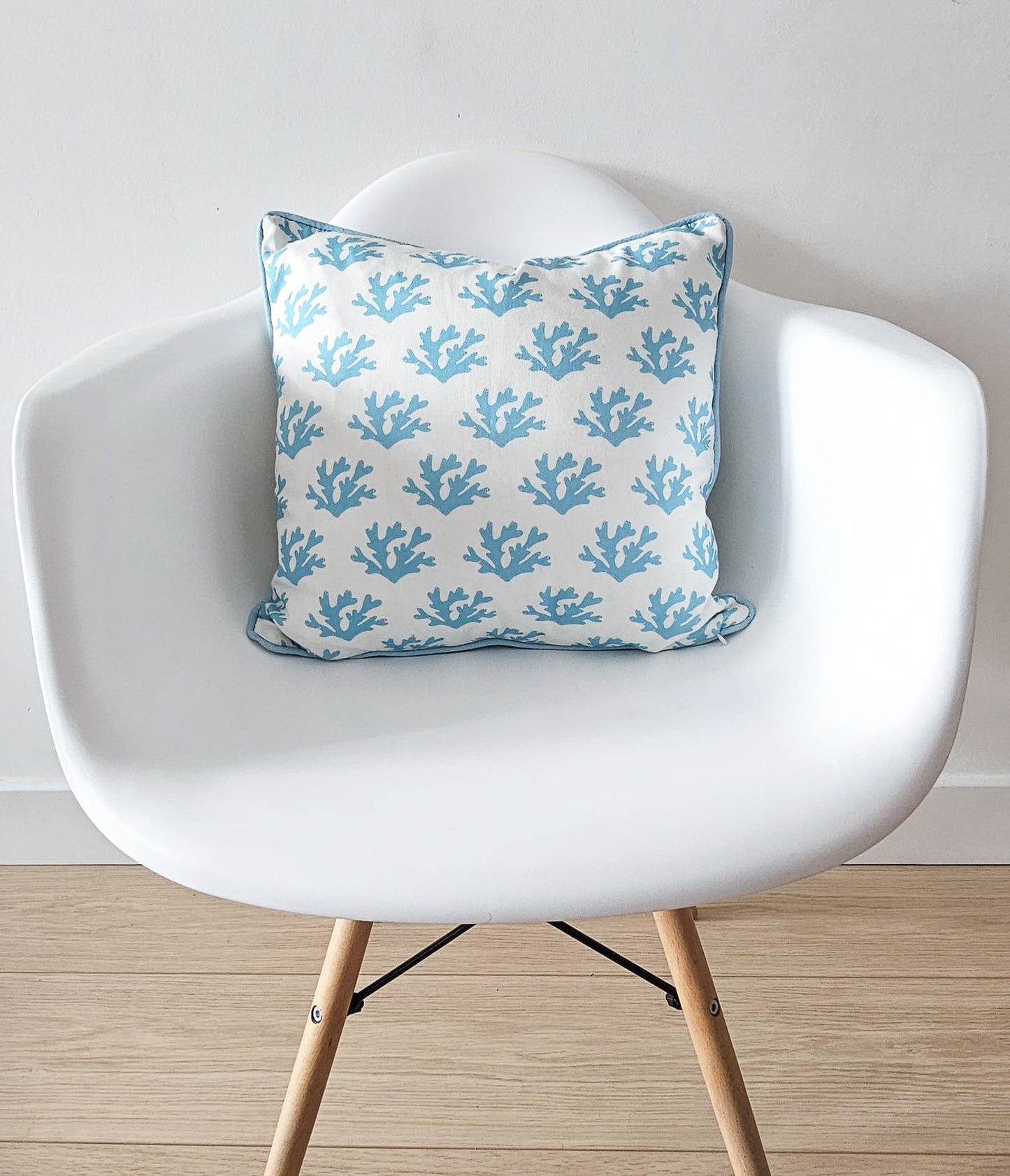 Blue seaweed print cushion by ZIA LIVING, featuring a white and blue coral motif with blue piping, styled on a modern white chair with wooden legs.