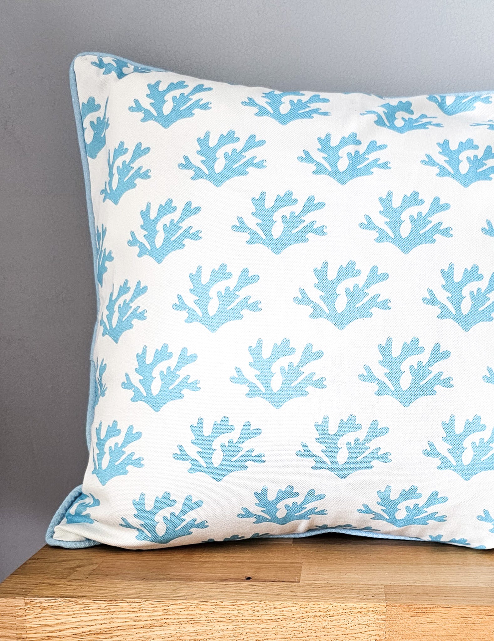 Sky blue seaweed print cushion by ZIA LIVING, featuring a white and blue coral motif with blue piping, styled on wooden shelf.