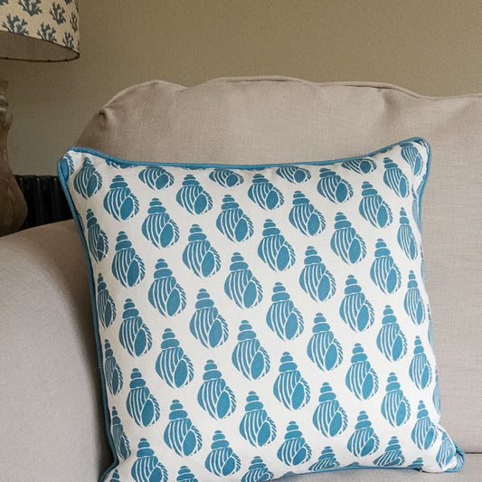 Sea Blue Shell cushion featuring a repeating hand‑carved shell motif in blue on a white background, photographed on a sofa— ZIA LIVING.