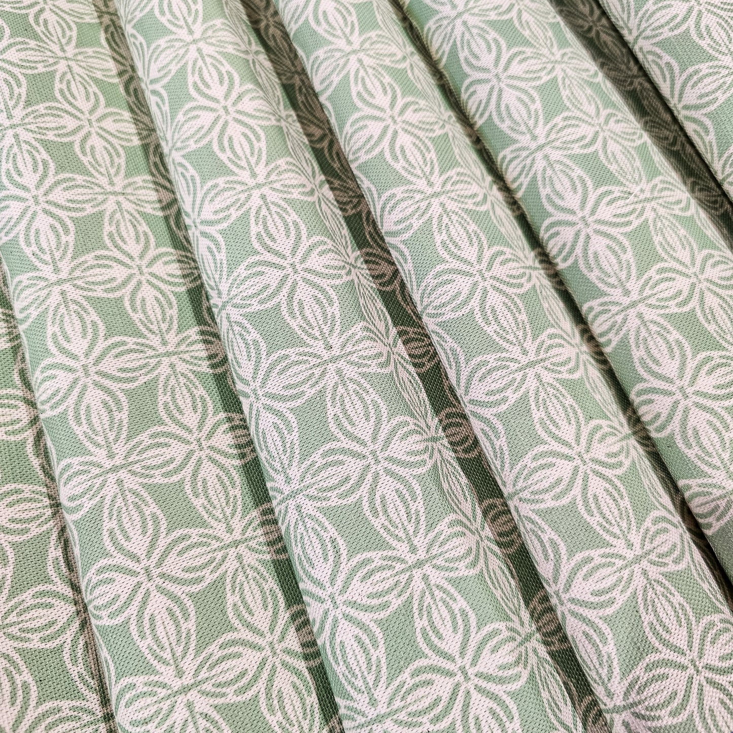 Bella cotton linen fabric featuring a repeating white interlocking lino print motif on a soft green background. ZIA LIVING