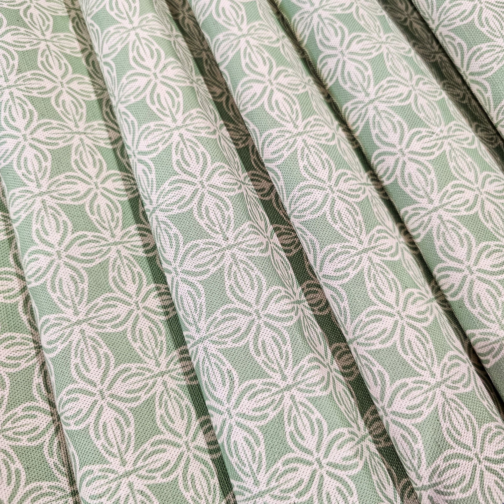 Bella cotton linen fabric featuring a repeating white interlocking lino print motif on a soft green background. ZIA LIVING
