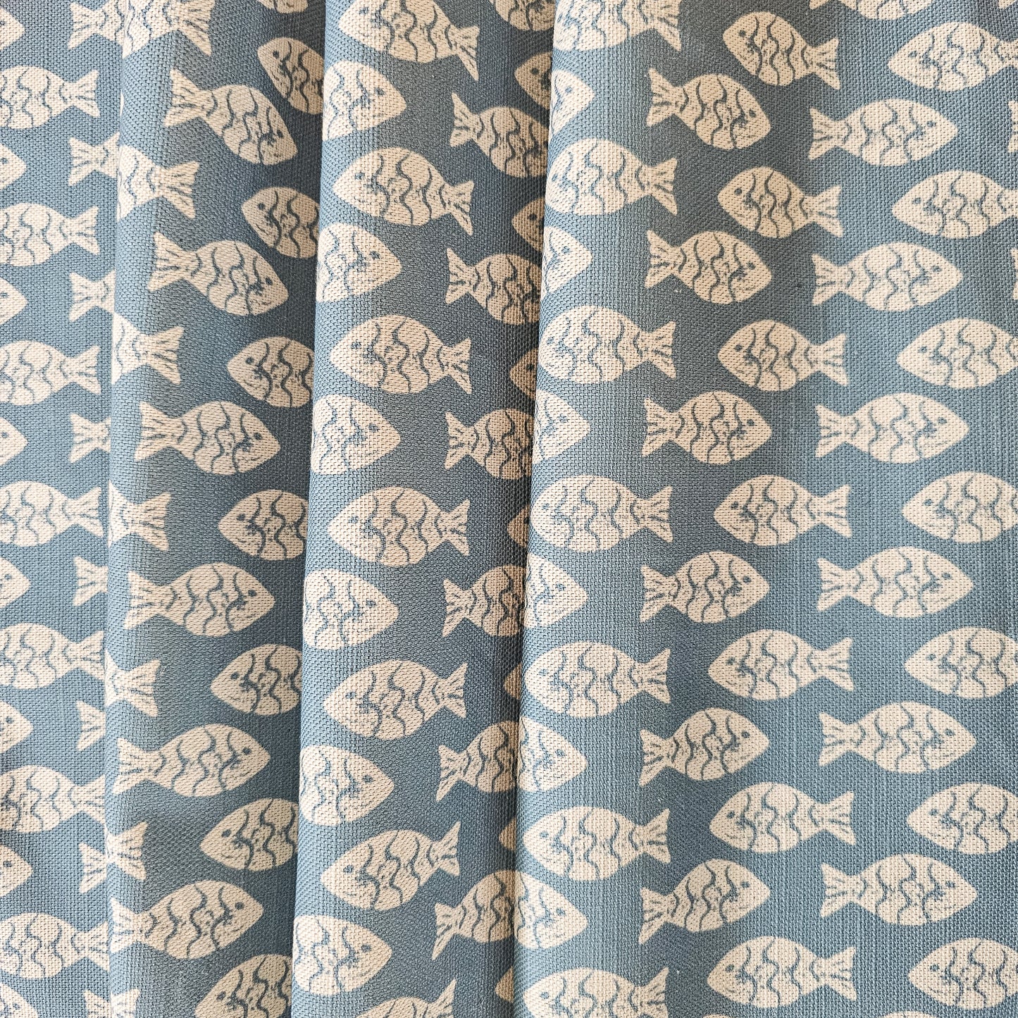 Zia Living Shoal lino print fish design fabric is blue.  Featured as draped fabric