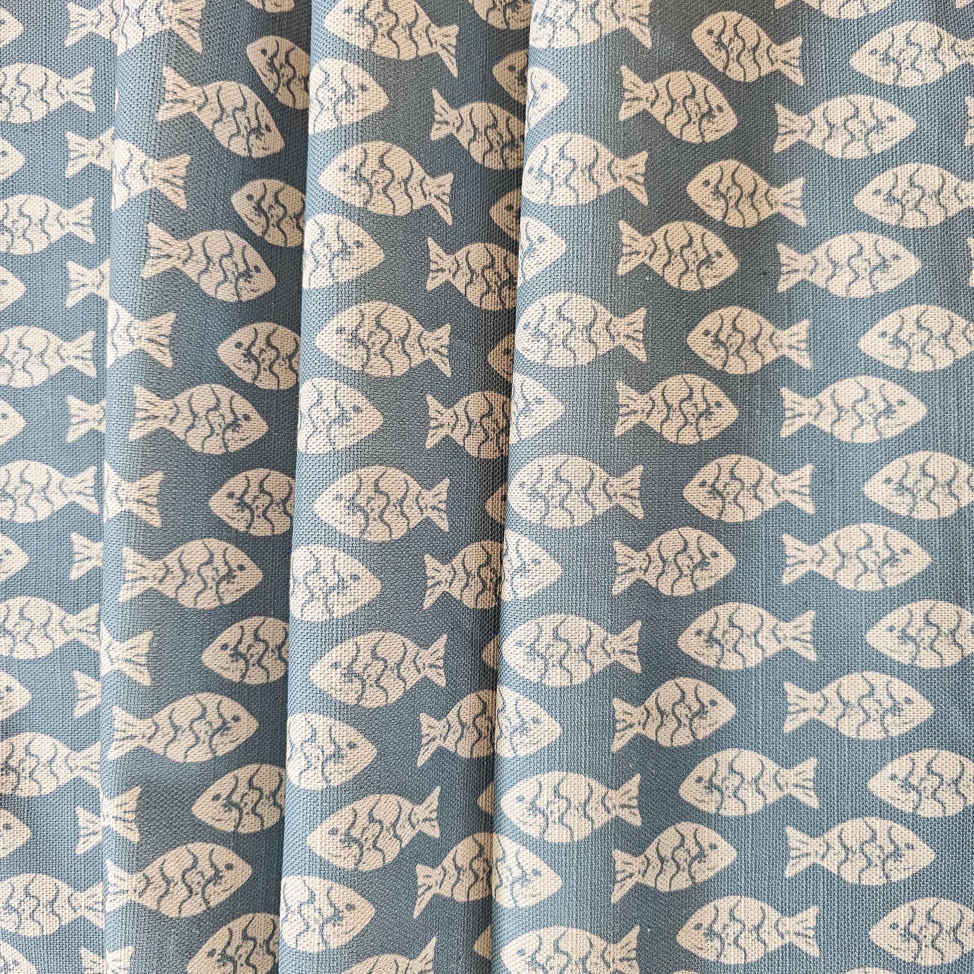 Zia Living Shoal lino print fish design fabric is blue.  Featured as draped fabric
