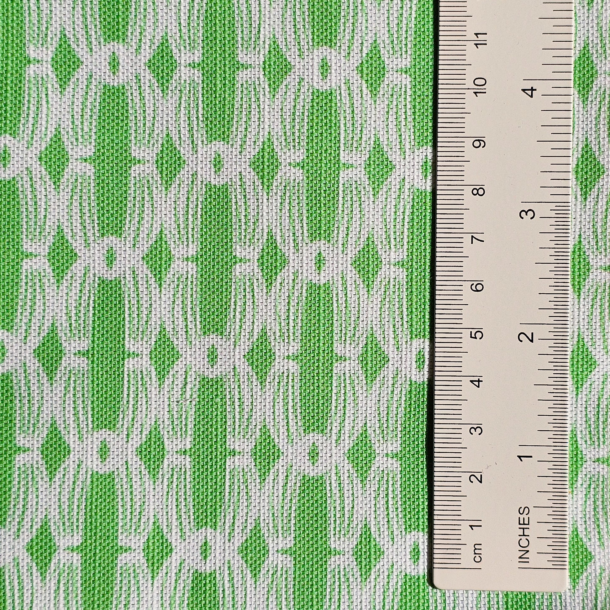 Close‑up of ZIA LIVING’s Anello cotton‑linen fabric in apple green and white, showing its interlocking oval and diamond geometric weave pattern and textured artisan finish. With ruler showing scale of pattern repeat.