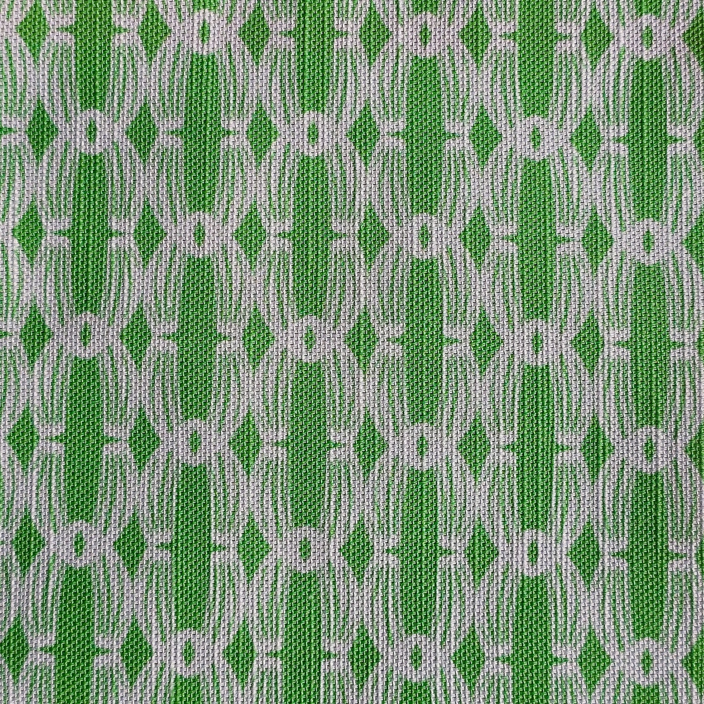 Close‑up of ZIA LIVING’s Anello cotton‑linen fabric in apple green and white, showing its interlocking oval and diamond geometric weave pattern and textured artisan finish.