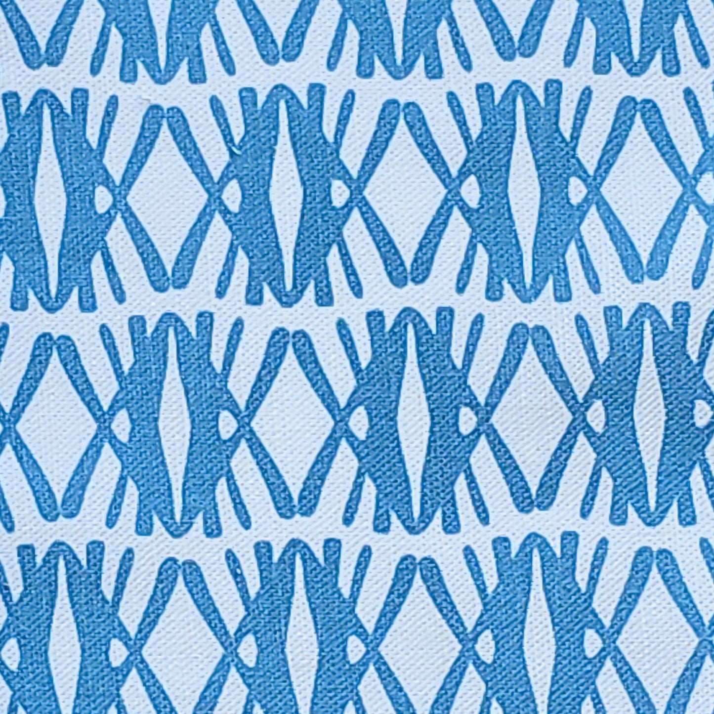 Seagrass cotton linen fabric featuring interlocking green and blue woven‑style motifs in a repeating geometric pattern on a white background. ZIA LIVING.