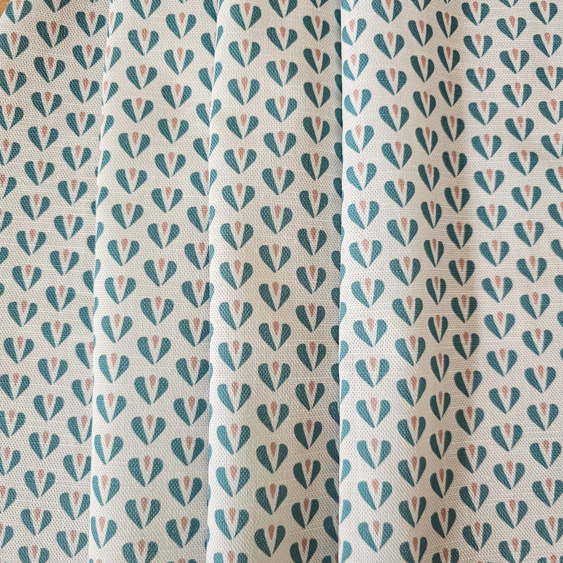 Carina, heart shaped motif in duck egg and pink colours on neutral fabric, shown as drapes, by Zia Living