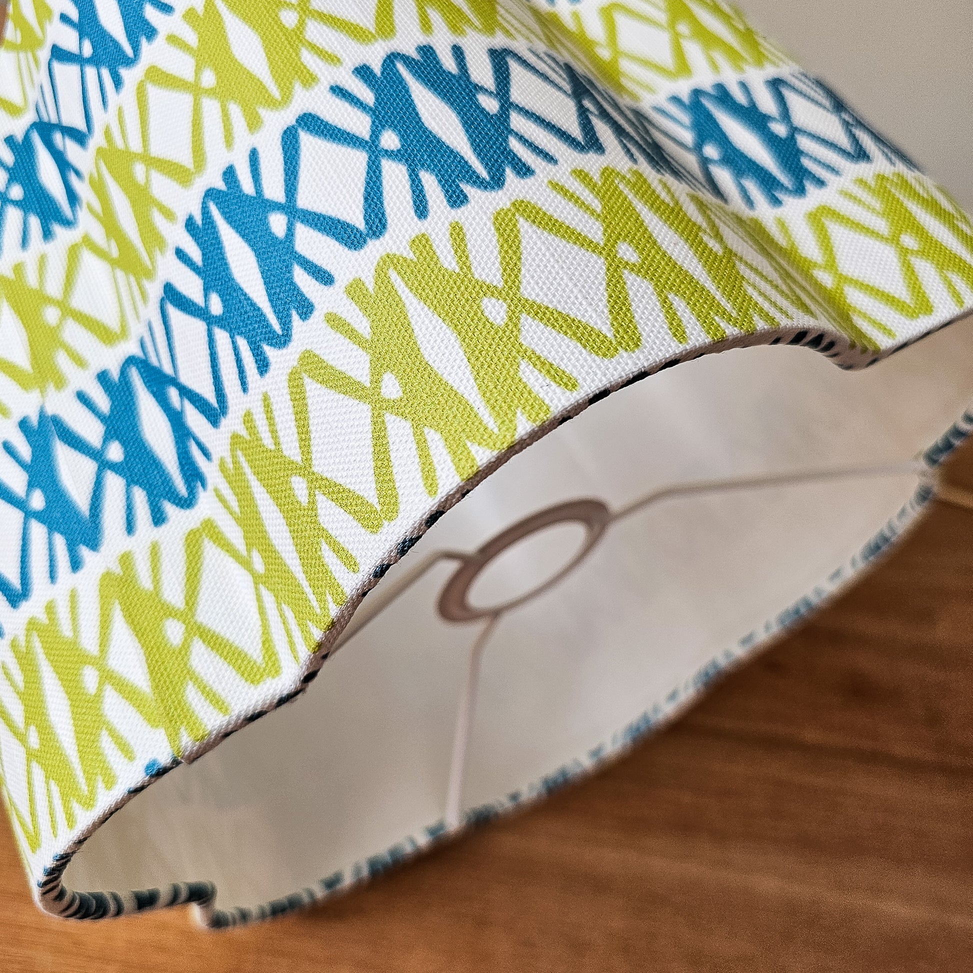 Seagrass print scalloped lampshade by ZIA LIVING, featuring a blue and green geometric lino‑print pattern on a white cotton‑linen shade with a wavy scalloped edge. Close up
