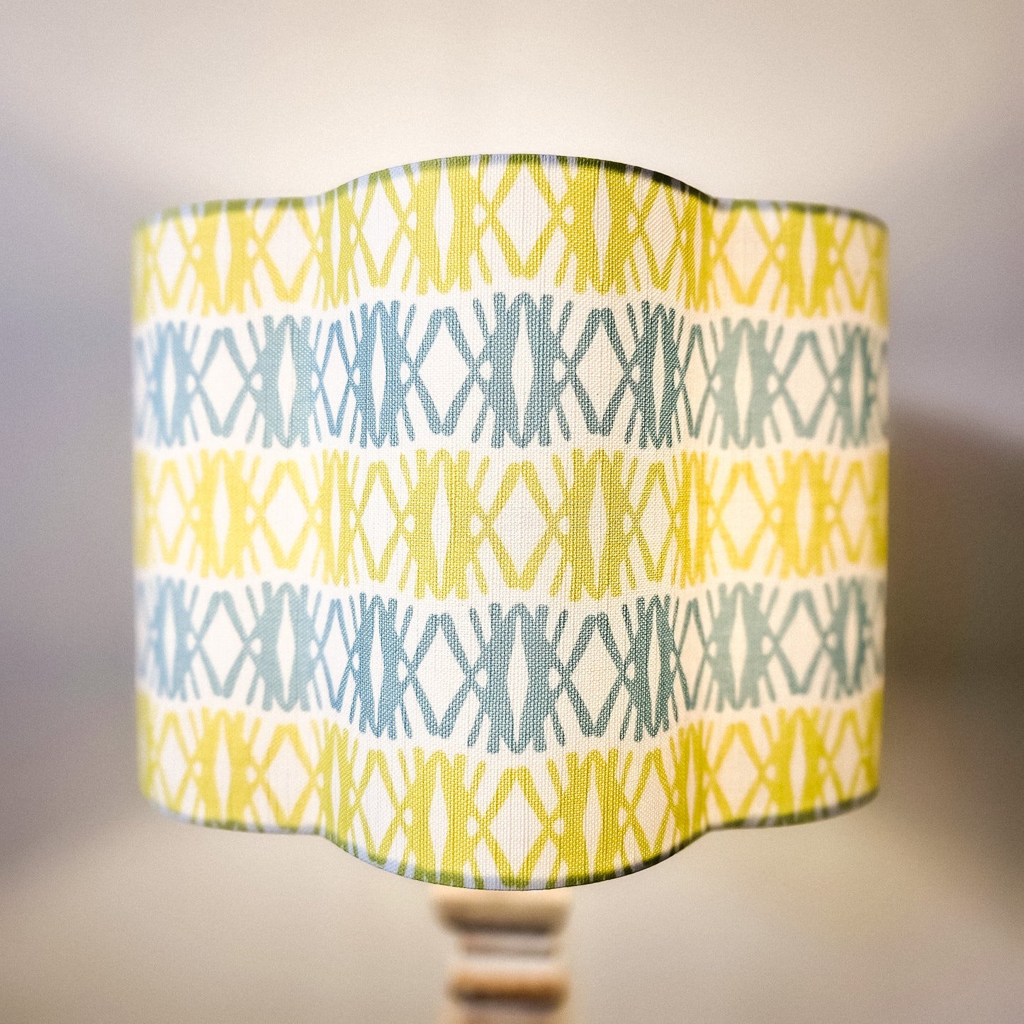 Seagrass print scalloped lampshade by ZIA LIVING, featuring a blue and green geometric lino‑print pattern on a white cotton‑linen shade with a wavy scalloped edge, feature as a lampshade - cosy view. 