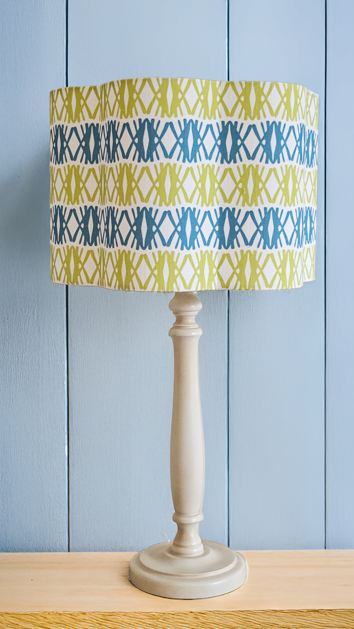 Seagrass print scalloped lampshade by ZIA LIVING, featuring a blue and green geometric lino‑print pattern on a white cotton‑linen shade with a wavy scalloped edge, feature as a lampshade with blue background.