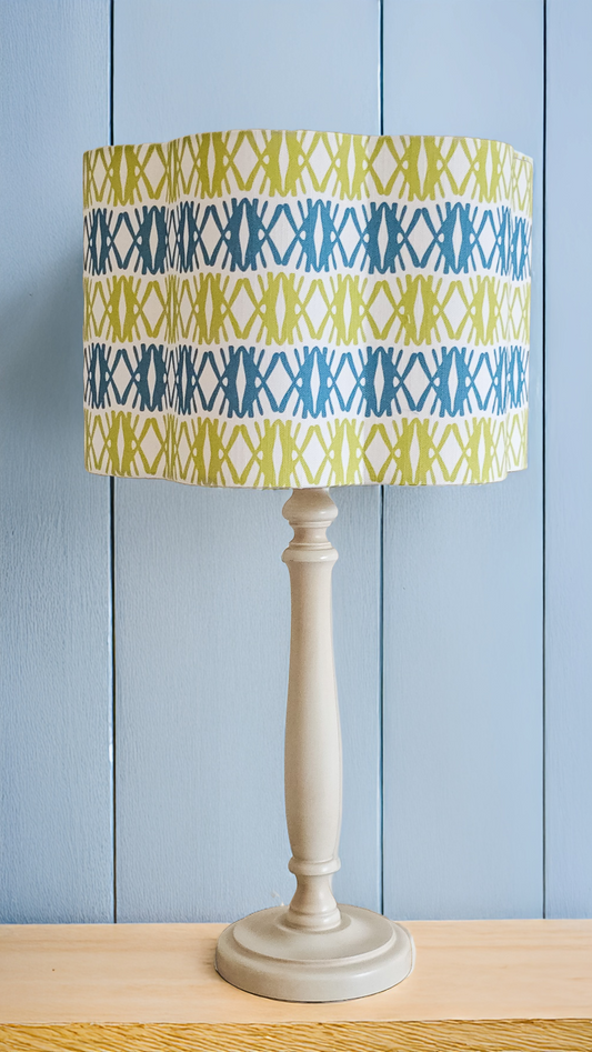 Seagrass print scalloped lampshade by ZIA LIVING, featuring a blue and green geometric lino‑print pattern on a white cotton‑linen shade with a wavy scalloped edge, feature as a lampshade with blue background.