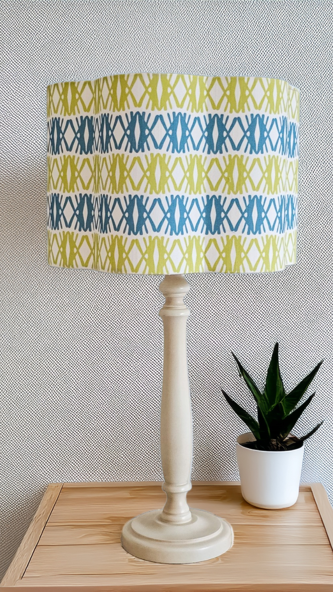 Seagrass cotton linen fabric featuring interlocking green and blue woven‑style motifs in a repeating geometric pattern on a white background, featured on a lampshade, with plant. ZIA LIVING.