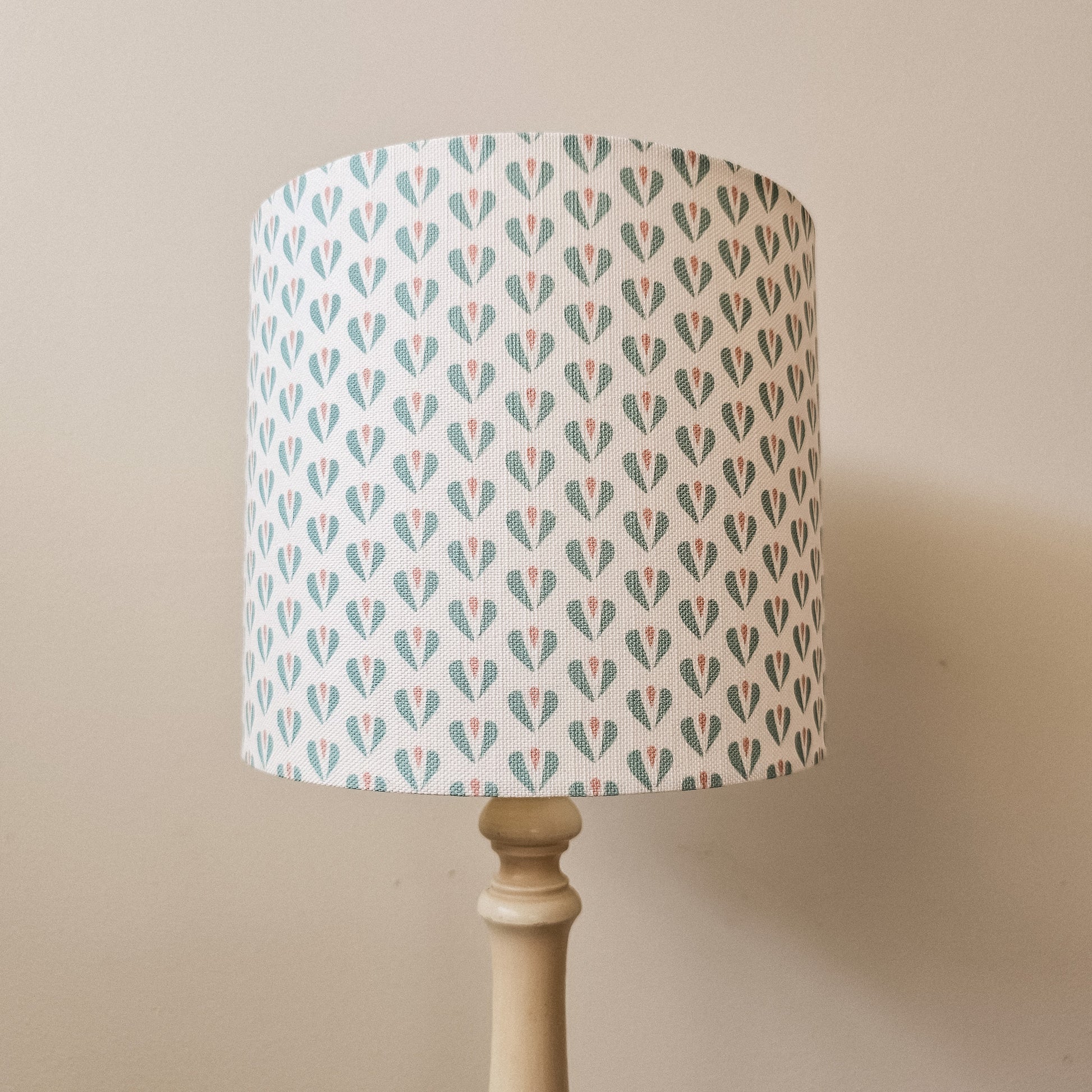 Heart motif lampshade by ZIA LIVING, featuring a repeating teal and pink pattern on a light cotton‑linen shade, styled on a wooden lamp base against a neutral wall.