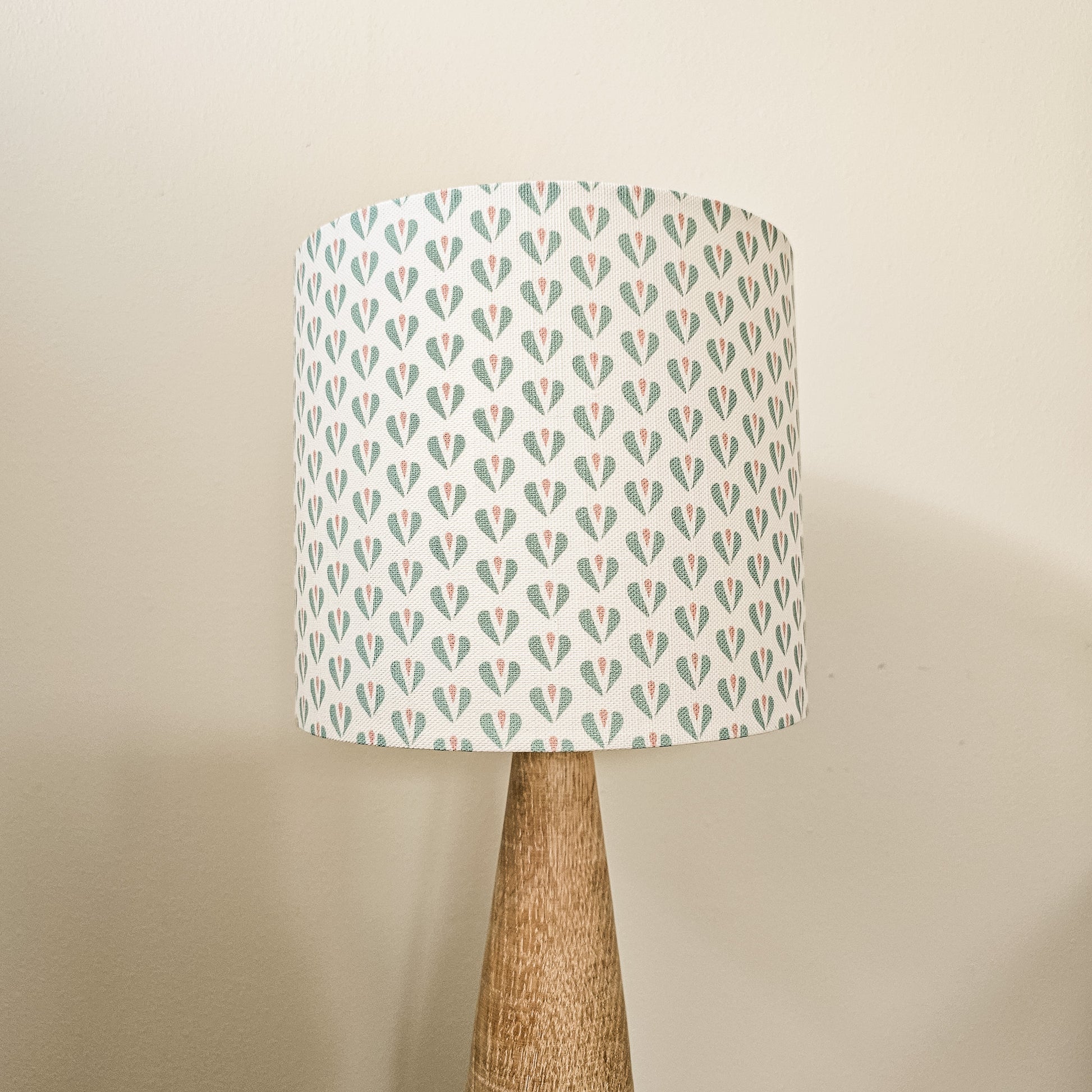 Heart motif lampshade by ZIA LIVING, featuring a repeating teal and pink pattern on a light cotton‑linen shade, styled on a wooden lamp base against a neutral wall.