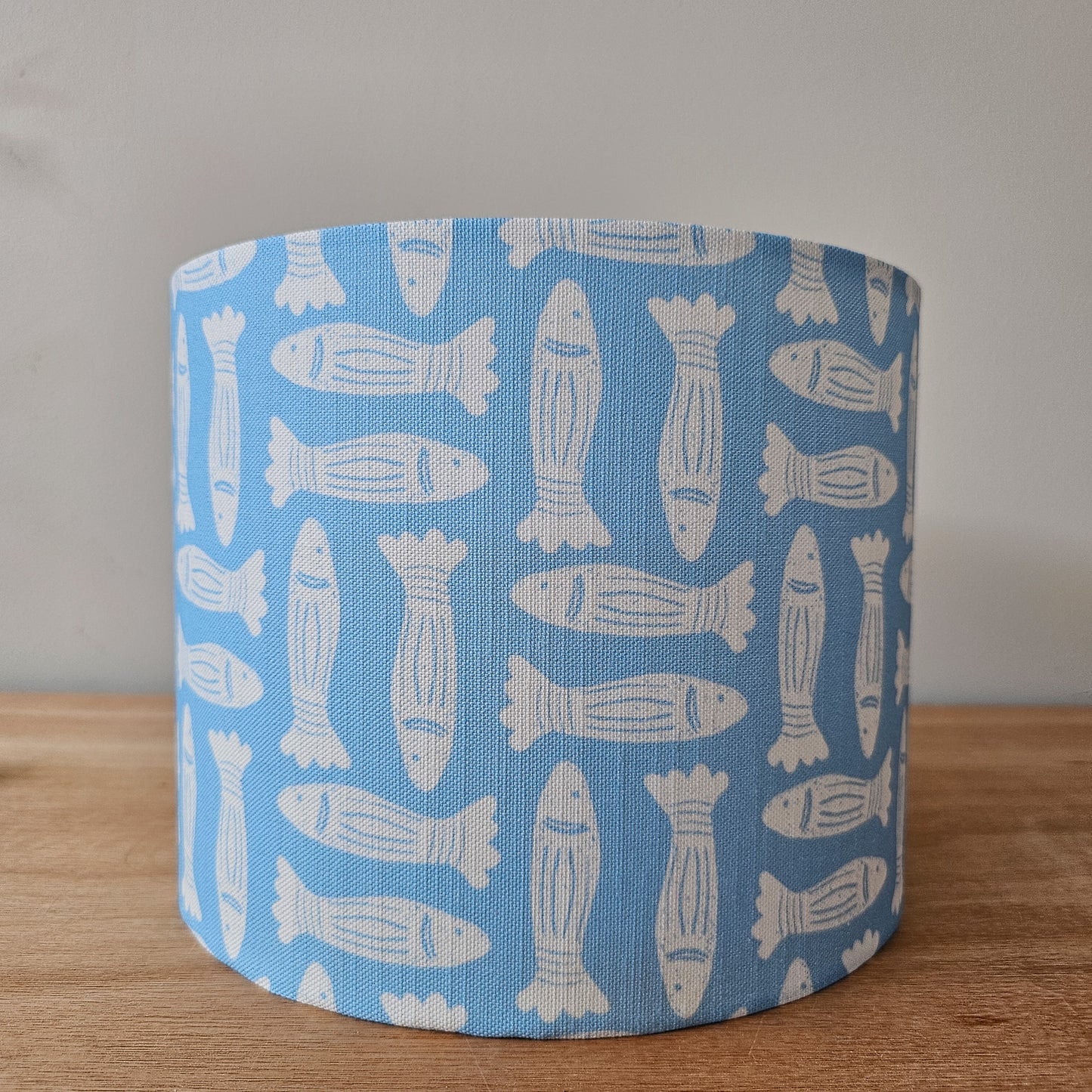 Zia Living Fishes fabric swatch lino print in sky blue with white fish featured on a drum lampshade