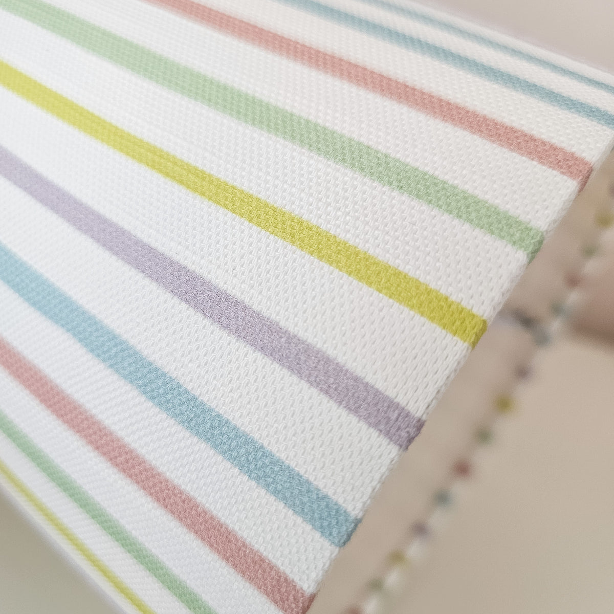 Close-up of a white with thin pastel rainbow stripes in green, yellow, purple, pink, and blue, lampshade