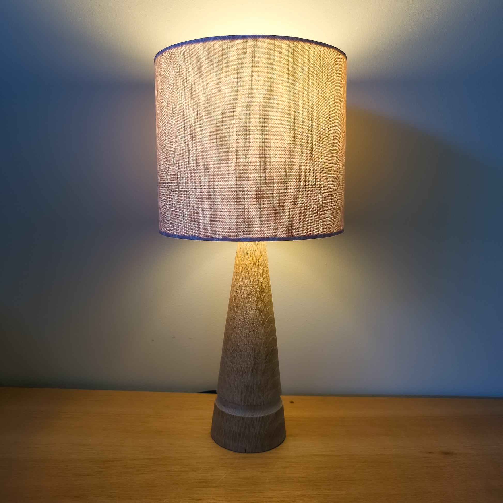 Powder Pink Rosemary cotton‑linen fabric featuring a lino‑style trellis pattern as a lampshade.  On a lamp in with a cosy light— ZIA LIVING.