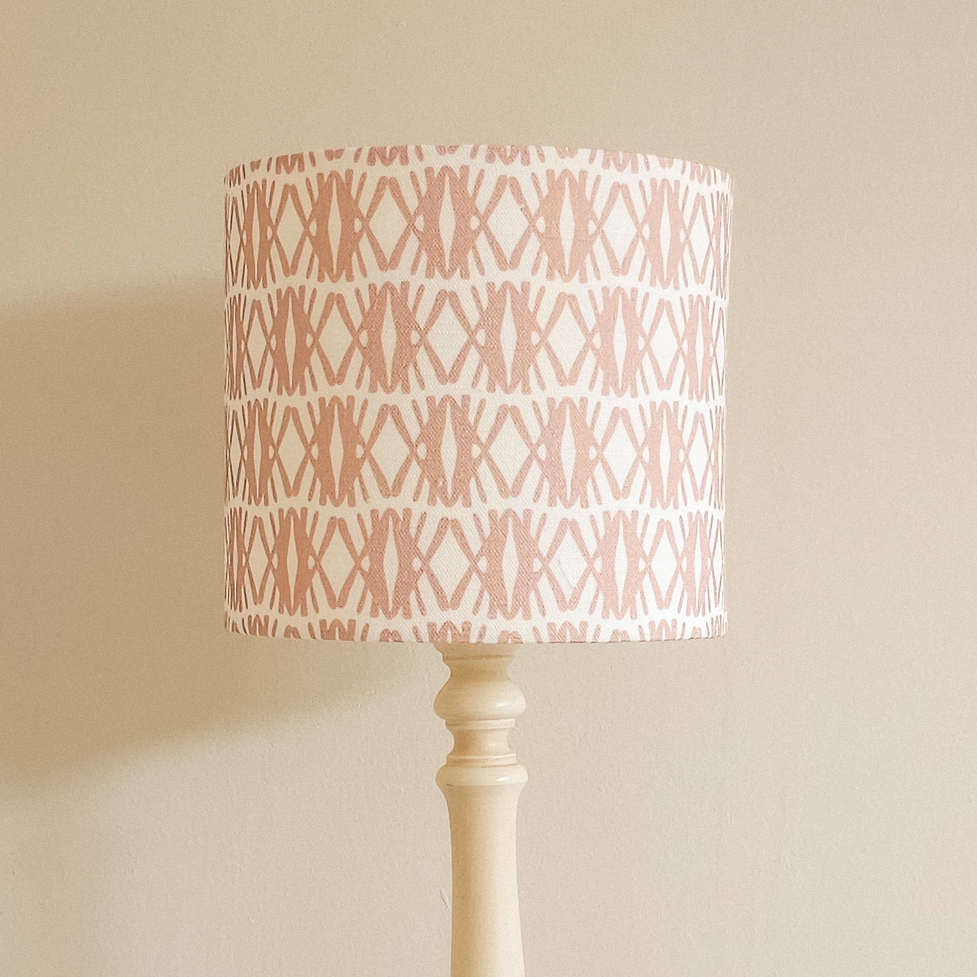 Seagrass cotton linen fabric featuring interlocking pink woven‑style motifs in a repeating geometric pattern on a white background, featured on a drum lampshade. ZIA LIVING.